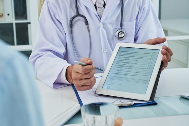 A doctor holding a tablet displaying an electronic health record (EHR) while discussing patient information, highlighting digital healthcare data security and HIPAA compliance.